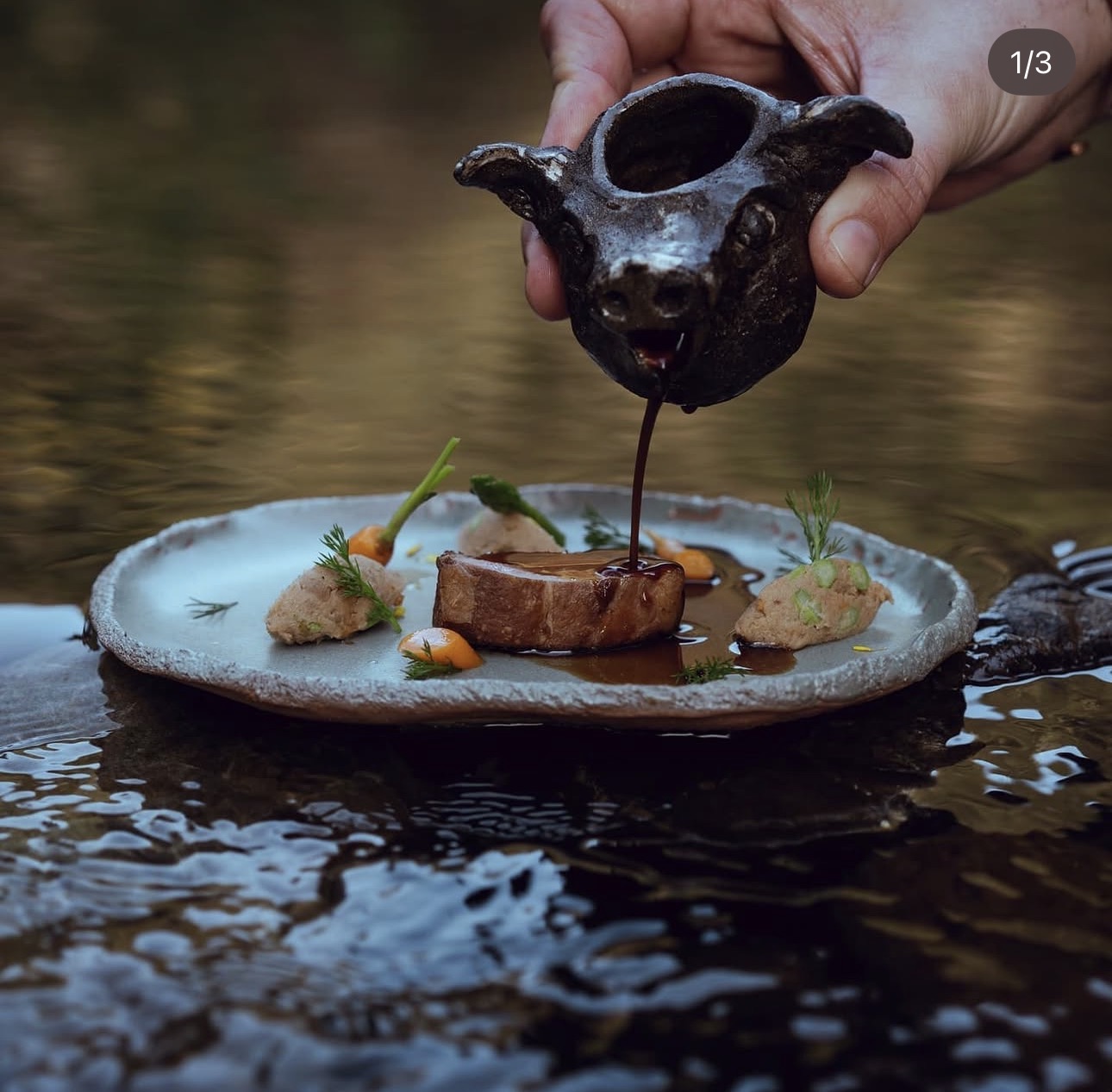 A Loki dish in a streambed with sauce being poured from a black ceramic pig-head vessel.
